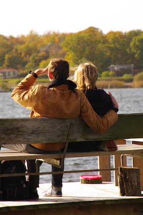 A couple sitting next to one another on a bench that overlooks a lake. 